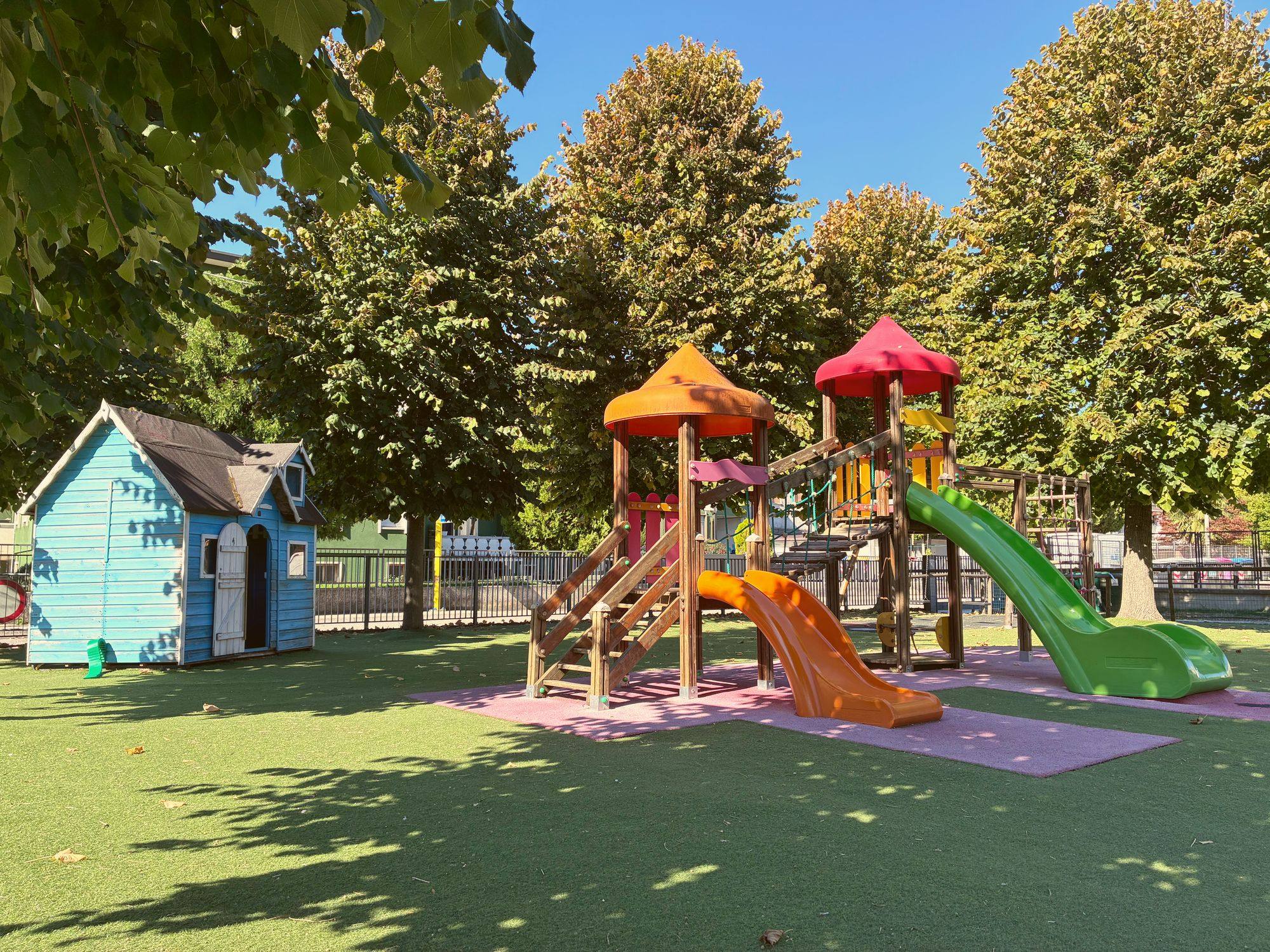 Giardino della scuola dell’infanzia con scivoli colorati e casetta in legno